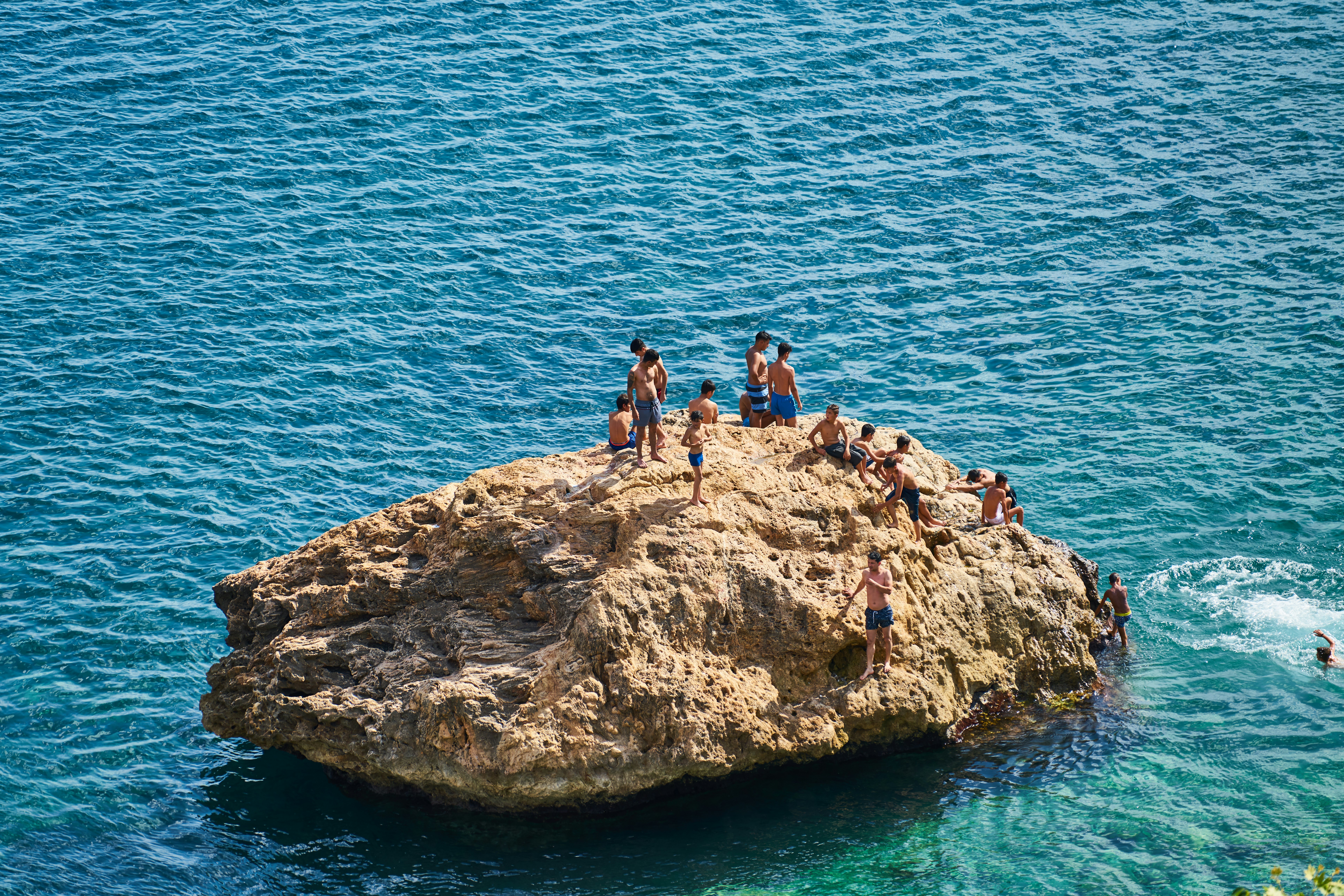 3 people standing on brown rock formation near body of water during daytime